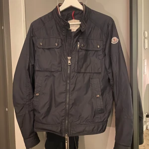 Intresse koll på marinblå moncler fieldjacket! - Säljer en snygg marinblå jacka från Moncler i mycket bra skick. Jackan har en dragkedja framtill och knappar på fickorna. Perfekt för höst och vår med sin stilrena design och bekväma passform. Den är långärmad och gjord i ett syntetmaterial som känns lätt och smidigt. Passar både till vardags och lite finare tillfällen. Den är i strl 2, bara att höra av sig vid frågor eller fler bilder. 