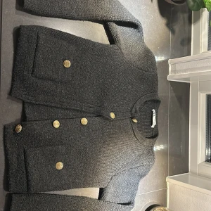 Grå stickad kofta från Zara - Säljer en stilren grå stickad kofta från Zara med dekorativa guldknappar. Koftan har långa ärmar och två små fickor framtill. Perfekt för kyliga dagar!