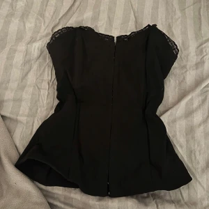 Svart korsett topp med spetsdetaljer xs - Svart korsett med spetsdetaljer längs halsringningen. Perfekt för en fest! Stl 34 och jätte fint skick 🩷