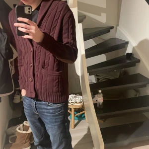 Cardigan  - Säljer en snygg vinröd kofta från GANT med knappar framtill och ribbade detaljer. Perfekt för kyligare dagar och ger en stilren look. Passar bra till jeans eller chinos. Ny pris 2000kr mitt pris 750kr