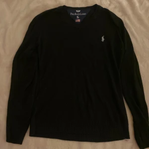 Svart tröja från Polo Ralph Lauren - Snygg svart tröja från Polo Ralph Lauren med v-ringning och broderad logga på bröstet. Perfekt för en stilren look. Tröjan har långa ärmar och är tillverkad i ett mjukt material. Köptes för ungefär 2 år sedan men har tröttnat på den med tiden som gått, priset kan diskuteras. Vid frågor eller funderingar skicka gärna ett pm.😃