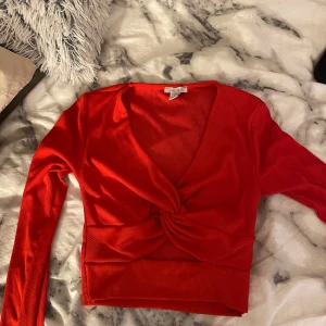Röd ribbad omlottopp - Snygg röd omlottopp med ribbad struktur och v-ringning. Toppen har långa ärmar och en knutdetalj framtill som ger en stilren look. Perfekt för att liva upp garderoben med en färgklick.