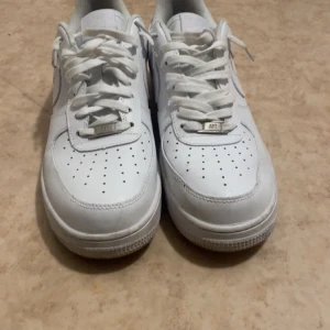 Vita Nike Air Force 1 sneakers - Säljer ett par klassiska vita Nike Air Force sneakers. Skorna har en stilren design med snörning och perforerade detaljer för ventilation. Perfekta för en avslappnad och trendig look. Använt endast ett par gånger  och kommer inte med originalbox tyvärr.