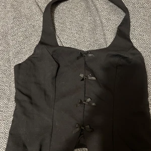 Svart korsettopp med rosetter - Snygg svart korsettopp med dekorativa rosetter framtill. stilren design som passar perfekt för en kväll ute.