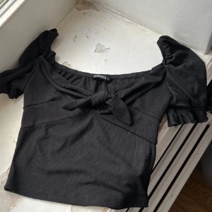 Svart ribbad topp från Shein - Snygg svart ribbad topp från Shein med korta puffärmar och en knytdetalj framtill. Perfekt för en trendig look.