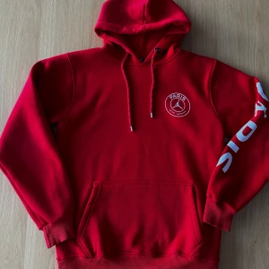 Röd hoodie Paris Saint-Germain - Snygg röd hoodie med Paris Saint-Germain-tryck i vitt. Hoodien har en stor logga på ryggen och text på ärmen. Perfekt för fotbollsfans som vill ha en bekväm och stilren look. Nypris 800 kr