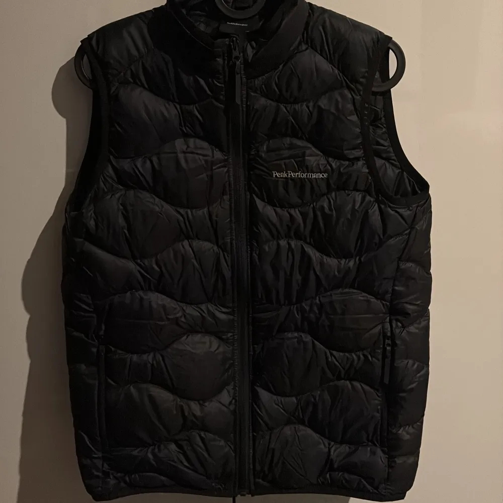 Snygg svart dunväst från Peak Performance med dragkedja framtill. Perfekt för kyligare dagar och ger en sportig look. Västen har en quiltad design och är idealisk för lager-på-lager-stil. Bra skick säljs billigt!!!! Perfekt julklapp!!!. Takit.