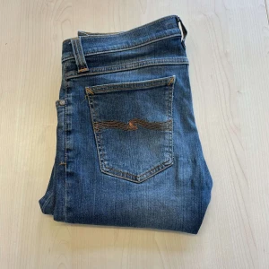 Nudie jeans - Snygga blå jeans med en tight passform och klassisk femficksdesign. Byxorna har en diskret tvättad look och orange sömmar som ger en cool kontrast. Perfekta för en avslappnad stil.