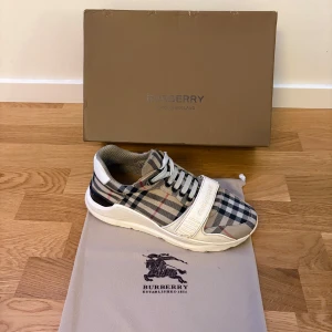  Burberry checked lace-up - Skorna har lite skador, dessa skor från burberry har inte den bästa kvaliten.. Snygg sneaker från Burberry med klassiskt rutigt mönster i beige, svart och vit. Skon har snörning och en bred rem över foten för extra stil och komfort. Perfekt för en trendig look. 
