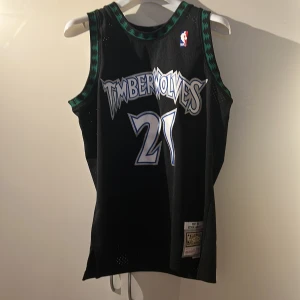 Svart Timberwolves basketlinne från Mitchell & Ness - Säljer ett svart Timberwolves basketlinne från Mitchell & Ness, del av deras Hardwood Classics-kollektion. Linnet har nummer 21 och namnet Garnett på ryggen. Perfekt för basketfans! 🏀