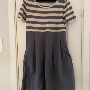 Gråa och beige randig klänning i strl M från COS - Gråa och beige randig klänning i strl M från COS.  Ny, aldrig använd. Då jag upptäckte en liten färgmiss på klänningen provade jag att tvätta den.   Klänningen har fickor i sidorna.  Mått Över bröstet: ca 46 cm Längd från axeln och ner: ca 94 cm  100% bomull   Kommer från ett djur och rökfritt hem.