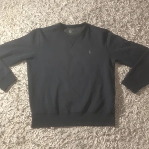 Mörkblå tröja från Polo Ralph Lauren - Säljer en stilren mörkblå tröja från Polo Ralph Lauren. Tröjan har långa ärmar och en liten broderad logotyp på bröstet. Perfekt för en avslappnad och klassisk look. 