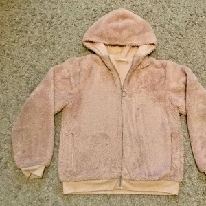 Rosa teddyjacka från KappAhl - Mysig och fluffig rosa teddyjacka från KappAhl. Perfekt för kyliga dagar med sin gosiga huva och dragkedja framtill. Superfin att ha på sig under hösten eller vintern. Använt skick,(se bilder) lite sliten på ena ärmen. Fickor framtill🩷