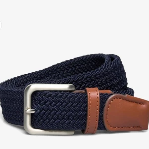 Mörkblått flätat bälte med bruna detaljer - Säljer ett snyggt mörkblått flätat bälte med stilrena bruna läderdetaljer. Bältet har ett silverfärgat spänne som ger en klassisk touch. Perfekt för både vardag och fest!
