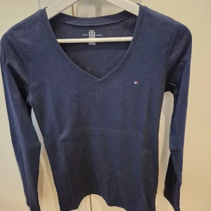Tröja Tommy Hilfiger - Tröja från Tommy Hilfiger. Marinblå färg. Nyskick, aldrig använd. V-ringad form. Mjuk och skön material, väldigt bekväm. Märke på höger sida. Storlek XS. 100% bomull. Axelbredd 36 cm, längd 63 cm.