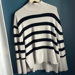 Svart/Vit stickad tröja  - Snygg randig tröja med hög hals. Tröjan är något längre baktill och har en avslappnad passform.