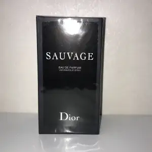 Säljer en helt ny och oöppnad flaska av Sauvage Eau de Parfum från Dior. Förpackningen är elegant och stilren i svart med vit text. Perfekt för den som vill ha en tidlös och maskulin doft. Passar både till vardags och fester! 100ml