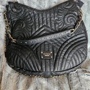Svart quiltad axelväska från Guess - välanvänd äkta guess väska.  Defekter/slitage finns.  Gör egen bedömning av bilderna 