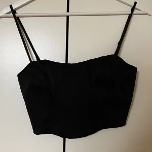 Svart korsettopp från Bershka - En kort åtsittande korsettopp i svart från Bershka. Använd sparsamt och är som ny. Enkel dragkedjestängning baktill! Passar perfekt till fest!