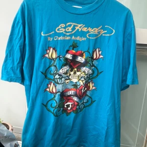 Blå Ed Hardy t-shirt med tryck - Blå oversized Ed Hardy t-shirt med tryck på fram- och baksidan. Den är i bra skick förutom att texten på framsidan är lite sprucken (syns på bild 3). 