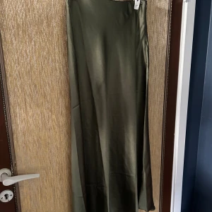 Olivgrön långkjol i satin - Säljer en superfin olivgrön långkjol i satin. Kjolen har en slät och glansig yta som ger en lyxig känsla. Perfekt för både vardag och fest! Den är i nyskick och har en normal passform. Passar perfekt till höst- och vårsäsongen. 🌿✨