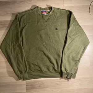 Grön sweatshirt från Champion - Säljer en grön sweatshirt från Champion i storlek L. Den har en klassisk design med ribbade muddar och en liten Champion-logga på bröstet. Perfekt för en avslappnad stil. Lite använd men i bra skick!