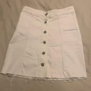Vit jeanskjol från Perfect Jeans - Säljer en superfin vit jeanskjol från Perfect Jeans i storlek 36. Kjolen har en rad med snygga knappar framtill och en rå kant nertill som ger en cool och avslappnad look. Perfekt för sommardagar eller en avslappnad fest! 🕶️