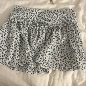 Blommig kjol från Gina Tricot - Säljer en superfin blommig kjol från Gina Tricot i storlek 146/152. Kjolen är vit med blå blommor och har en söt volangdetalj upptill. Perfekt för sommarens alla äventyr! 🌸