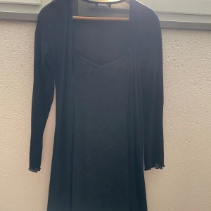 Svart långklänning från Linnea - Säljer en elegant svart långklänning från Linnea. Klänningen har ett subtilt blommigt mönster och är tillverkad i ett lätt och flödande material. Klänningen kommer med en lång kofta till, och har en diskret slits framtill för extra rörelsefrihet. Står inte storlek men jag som vanligt vis är en M skulle säga att den är just en M/S.  Perfekt för fest tillfällen!💓