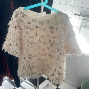 Vit paljettprydd topp från Zara - Säljer en superfin vit tröja från Zara med massor av paljetter och fluffiga detaljer. Jag säljer denna tröja för att den inte kommer till användning. Tröjan är köpt på plick men är i bra skick!😇💗