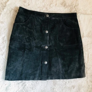 Svart mocka-kjol - Snygg skinnkjol från Jofama, str 42.  Sparsamt använd. Mycket fina detaljer på knapparna. Praktiska fickor.  