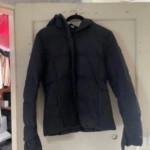 Svart pufferjacka från North Sails - Säljer en svart pufferjacka från North Sails i storlek M. Jackan är perfekt för kalla dagar med sin vadderade design och har en praktisk huva. Den är långärmad och har en stilren look som passar till det mesta. Perfekt för både höst och vinter!