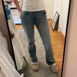 Lågmidjade jeans - Det är ett par lågmidjade, ljus blåa jeans med ett hål på ena knät. Dom är utsvängda och super fina! Bra material och skick! 