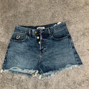 Jeansshorts från Lois - Säljer ett par snygga jeansshorts från Lois. De är högmidjade med en cool fransig kant längst ner. Shortsen har en knappgylf med fyra knappar och klassiska femficksdesign. Perfekta för sommaren!
