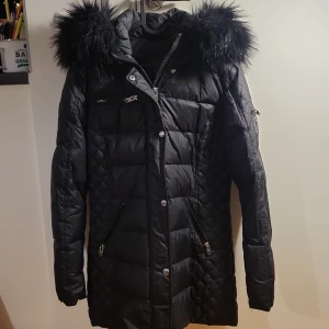 Svart dunjacka från Rockandblue - Säljer en snygg svart dunjacka från Rockandblue i storlek 40. Jackan har en fluffig pälsdetalj på huvan och stängs med dragkedja och knappar. Perfekt för kalla vinterdagar! 🖤