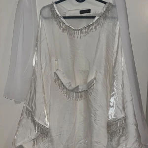 Vit långklänning med sjal.  - En fin lång abayaklänning som passar perfekt till fester eller förlovning. Kommer med en  vit sjal. Helt ny och oanvänd med prislapp på. 