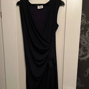 Mörkblå klänning från Isay - Snygg mörkblå klänning från Isay i ett mjukt och bekvämt material. Perfekt för både fest och vardag. Klänningen har en elegant drapering framtill och är ärmlös. Strl S. Sparsamt använd så bra skick.