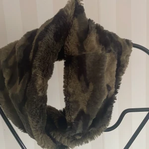 Mjuk halsduk i kamouflagemönster - Säljer en supermjuk och fluffig halsduk i ett coolt kamouflagemönster. Perfekt för att hålla sig varm under höst och vinter. Den har en härlig grön och brun färgkombination som passar till det mesta. Perfekt accessoar för att ge din outfit lite edge! 🧣