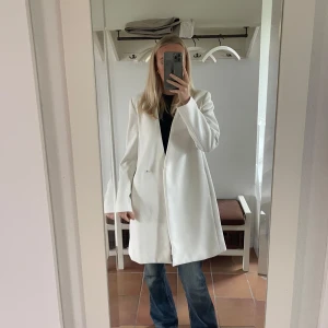 Vit kappa från Zara Basic - Säljer en stilren vit kappa från Zara Basic i storlek M. Den har en elegant design med långa ärmar och en enkel knäppning framtill. Perfekt för både vår och höst, och funkar lika bra till vardags som till fest. 🕊️