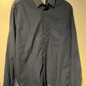 Mörkblå skjorta från Acne - Säljer en stilren mörkblå skjorta från Acne i storlek 50. Skjortan har en klassisk krage och knappar framtill. Perfekt för både vardag och festliga tillfällen. Den är i mycket bra skick och passar bra till höst- och vårsäsongen.