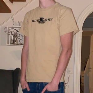 Burberry T-shirt - Säljer en snygg beige t-shirt från Burberry i bra skick. Den har ett klassiskt tryck på framsidan med Burberry-loggan. Perfekt för en avslappnad stil och passar till både jeans och shorts. Storleken är herr M och materialet känns som mjuk bomull. Perfekt för fest och normal användning, T-shirten är i 10/10 skick och endast andvänd ett fåtal gånger. Skriv gärna vid intresse❤️🙌