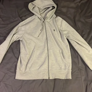 Grå hoodie från Polo Ralph Lauren - Säljer en stilren grå full zip från Polo Ralph Lauren väldigt bra skick och sparsamt använd.  Strl M. Nypris 1700 kr. Fråga gärna vid funderingar 
