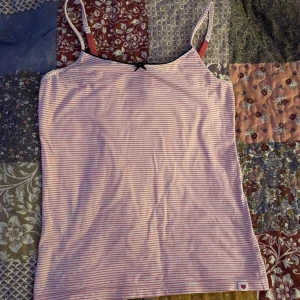 Rosa och vit randig linnetopp - Säljer en söt rosa och vit randig linnetopp. Toppen är i ett mjukt och bekvämt material, perfekt för sommardagar. Den har en liten etikett med ett hjärta längst ner. Passar bra till jeans eller shorts.