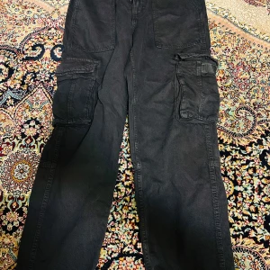 Svarta cargobyxor från Bershka - Säljer ett par svarta cargobyxor från Bershka i storlek 38. De har flera praktiska fickor och en loose passform som ger en avslappnad stil. Perfekta för höst och vår, och de funkar lika bra till vardags som till en casual utekväll. Materialet känns slitstarkt och bekvämt. 🖤
