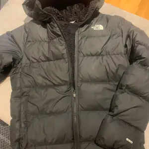 Säljer en svart dunjacka från The North Face i storlek XL junior . Jackan är perfekt för kalla vinterdagar med sitt varma dunfoder. Den har en dragkedja framtill och en mysig huva. Jackan är i mycket bra skick och redo för nya äventyr! 🖤