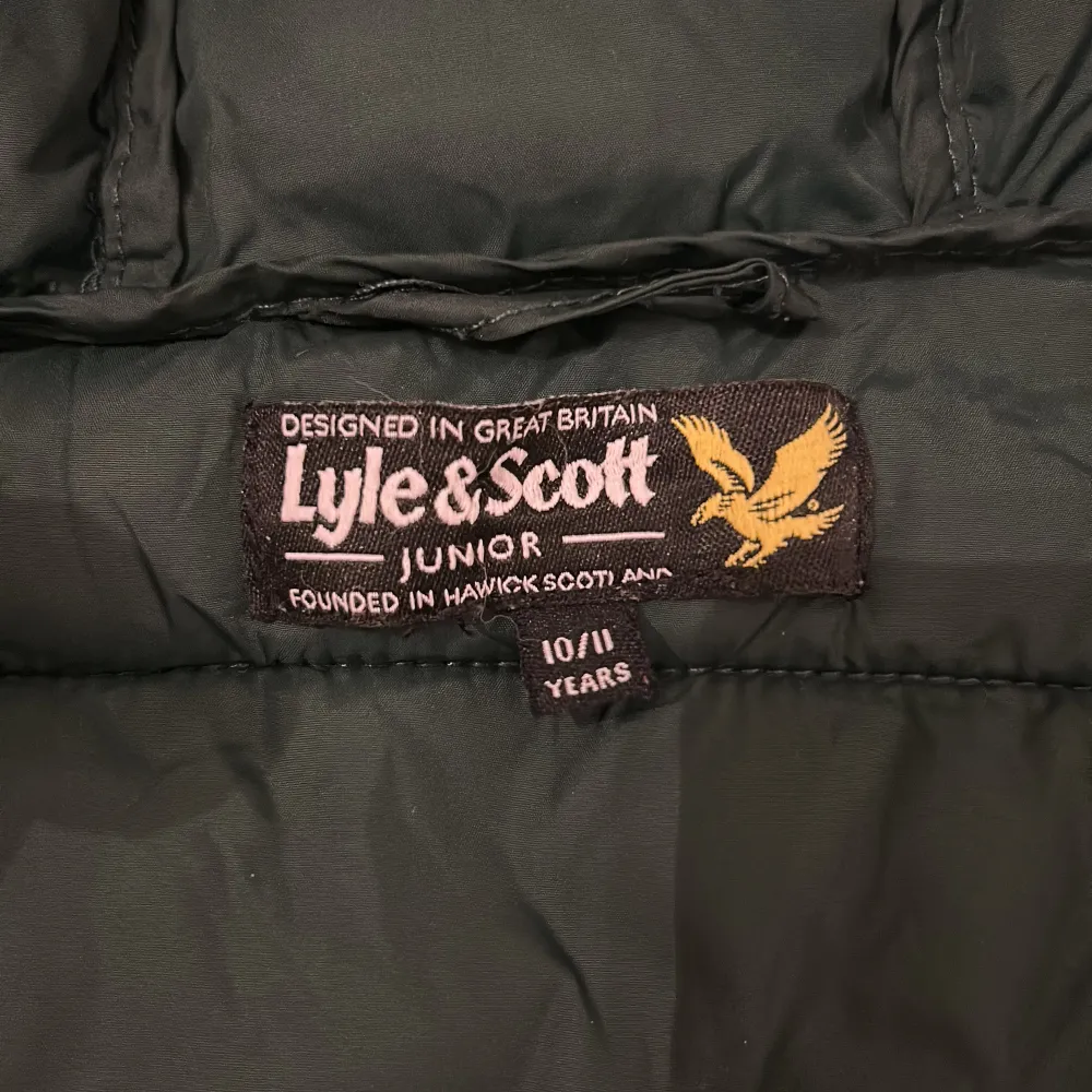 Säljer en grön pufferjacka från Lyle & Scott i storlek 10/11 år. Jackan har en mysig huva och dragkedja framtill. Perfekt för kyliga dagar! Den är i bra skick med en liten reva vid ärmslutet som går och fixa med några stygn. Passar både höst, vår och vinter.. Jackor.