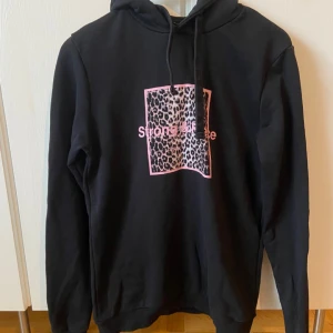 Svart hoodie med leopardmönster - Säljer en svart hoodie med ett coolt leopardmönster och texten 'Strong & Free' i rosa på bröstet. Den har en klassisk passform med långa ärmar och en bekväm huva med dragsko. Perfekt för en avslappnad stil eller en chill dag hemma. 🖤🐆