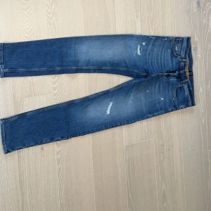 Två par jeans i olika tvättar - Säljer två par jeans i olika tvättar. Det första paret är ljusblå med slitningar. Det andra paret är mörkblå. 