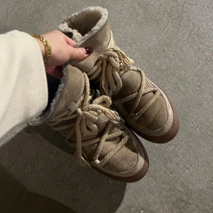 Beige boots från Inuikii - Säljer ett par snygga och varma boots från Inuikii i beige mocka och skinn. De har en mysig pälsfodring och rejäla snören för en cool look. Perfekta för vintern och hösten! De är i ett helt okej skick med slitage på hälen samt en svart fläck där bak. Nypris är 2999kr