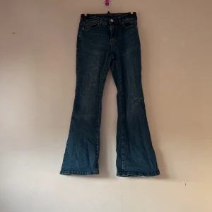 Blå bootcut jeans - Snygga blå bootcut jeans med klassisk femficksdesign och knappgylf. Perfekta för en avslappnad stil med en touch av retro. Passar bra till både sneakers och boots.